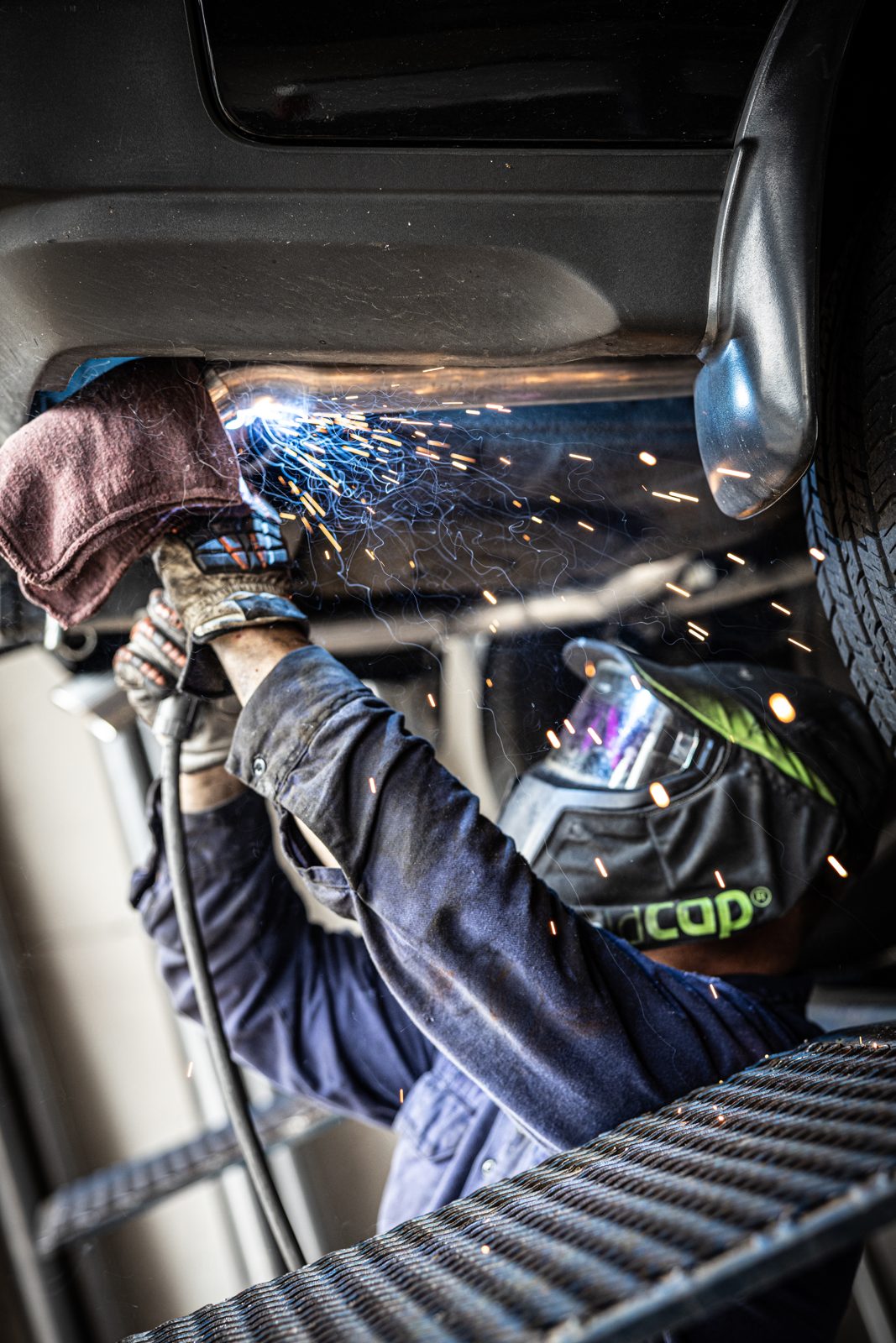 Technician MIG welding with flying sparks in a collision repair shop